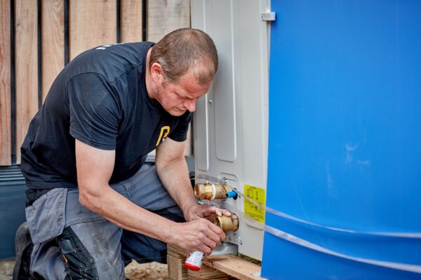An engineer installing pipe connections on an outdoor air source heat pump unit