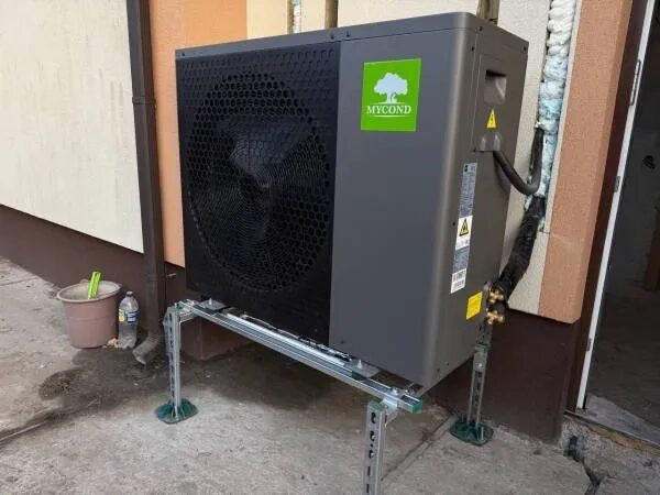 A Mycond BeeHeat air source heat pump outdoor unit installed on a metal stand against the exterior wall of a house
