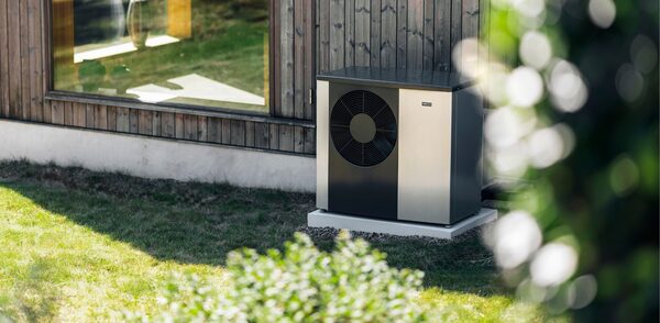A NIBE air source heat pump installed outside a timber-clad house on a gravel base beside a lawn