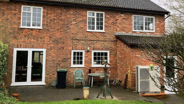 A Panasonic air source heat pump unit installed on the patio outside a brick house