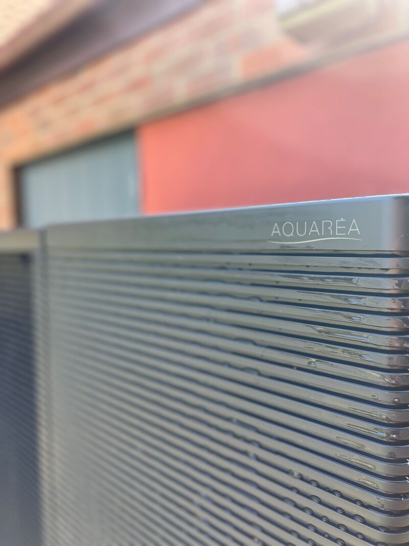A close-up of a Panasonic Aquarea air source heat pump outdoor unit installed outside a brick house