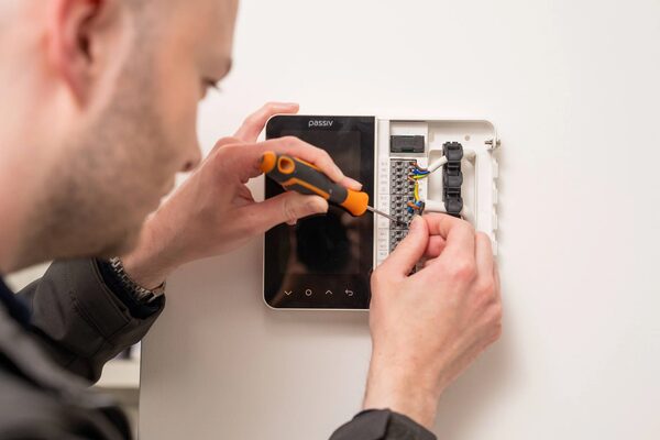 A technician wiring a Passiv smart thermostat on a wall with a screwdriver