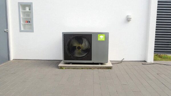 A Mycond monobloc air source heat pump unit installed on a concrete slab outside a white building