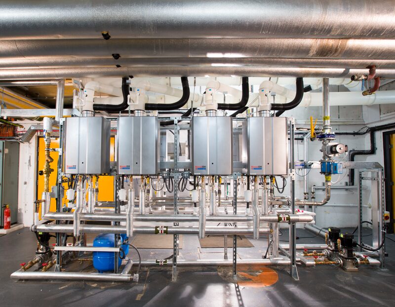 A bank of four Rinnai commercial water heating units installed on a manifold in a plant room