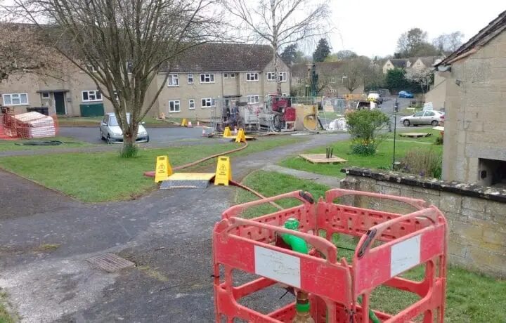 Ground works for a heat pump installation on a residential estate, with drilling equipment, hoses and safety barriers around a housing block