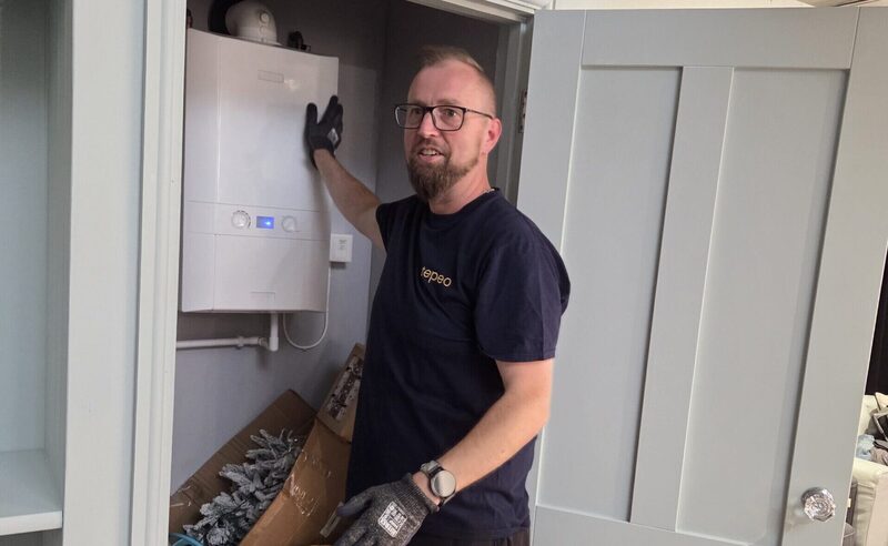 A tepeo engineer in a branded t-shirt installing a white ZEB heat battery boiler in a household airing cupboard