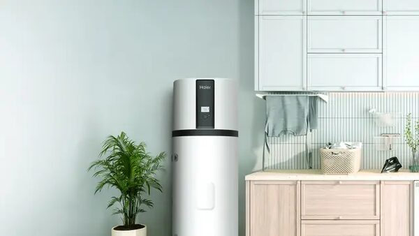 A white Haier hot water cylinder installed in a utility room next to a plant and kitchen cabinets