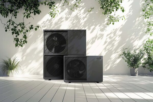 Two Grant air source heat pump outdoor units standing on a white decked patio against a sunlit wall with plants