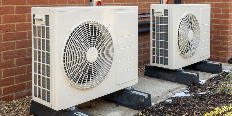 Two air source heat pump units installed outside against a brick house wall
