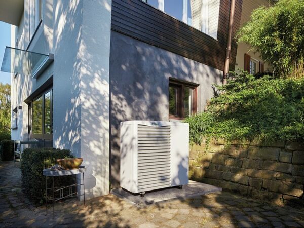 A Vaillant aroTHERM air source heat pump unit installed outside a modern house beside a garden wall