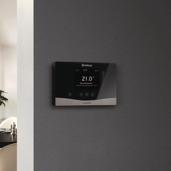 A Vaillant sensoCOMFORT smart thermostat mounted on a dark grey wall showing a set temperature of 21.0°C.