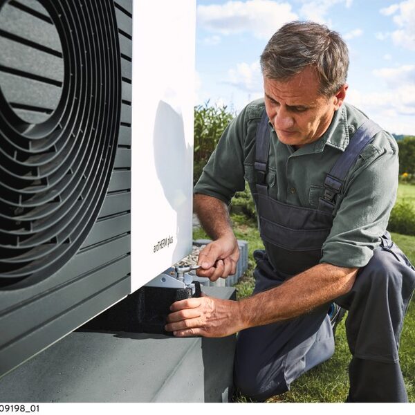 A technician in overalls working on an outdoor Vaillant aroTHERM plus air source heat pump unit in a garden