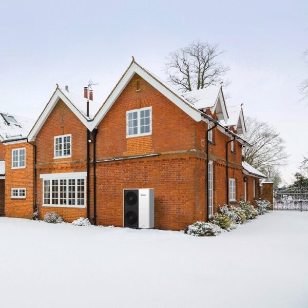 A Vaillant air source heat pump installed on the outside wall of a snow-covered brick house in winter