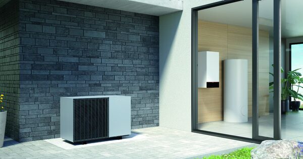 A Viessmann air source heat pump unit installed outside a modern house next to a glass wall showing an indoor hot water cylinder