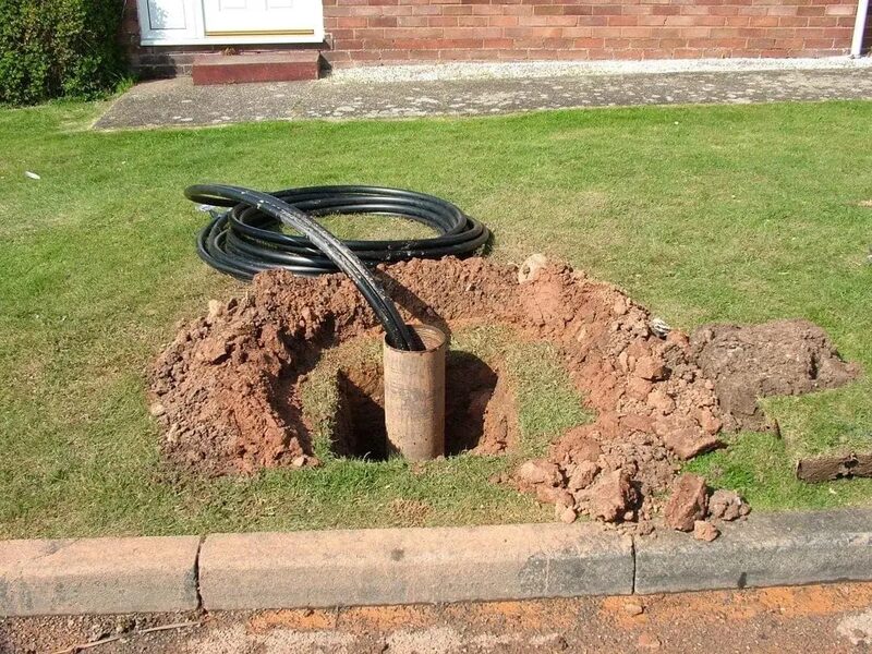 A ground loop pipe being installed into a drilled borehole in a grass front garden during ground source heat pump works