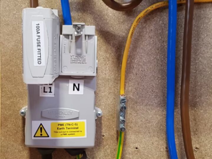 A Wylex electricity meter cut-out and PME earth terminal with incoming supply cables mounted on a board, labelled 100A fuse fitted