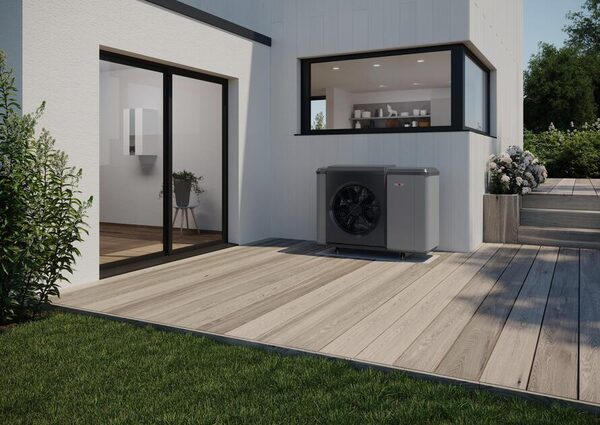A Wolf monobloc air source heat pump installed outside a modern white house on a wooden terrace