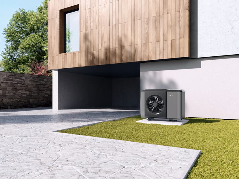 A Wolf CHA Monoblock air source heat pump unit installed outside a modern house on a grass patch beside a paved driveway
