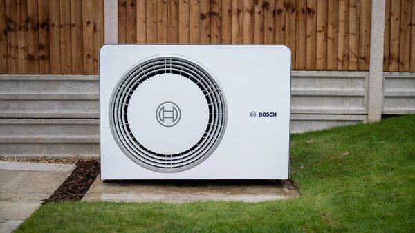 A white Bosch air source heat pump unit installed outdoors on a concrete base beside a lawn and wooden fence