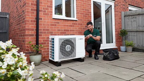 An engineer servicing a Worcester Bosch air source heat pump outside a red brick house