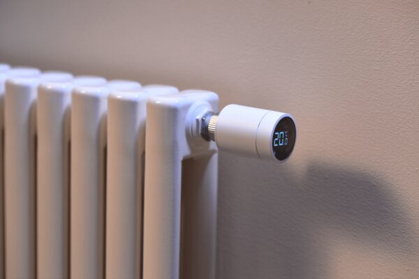 A white smart thermostatic radiator valve with a digital display reading 20°C fitted to a white panel radiator