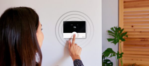 A woman adjusting a Baxi wireless smart thermostat mounted on a wall, showing 19 degrees
