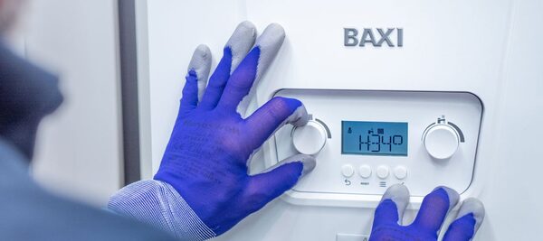 A gloved engineer adjusting the controls of a white Baxi gas boiler