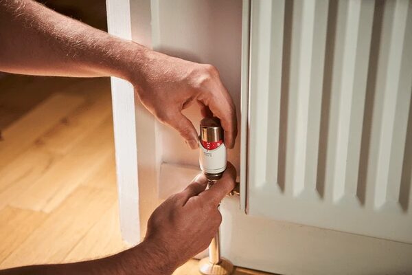A person fitting a thermostatic radiator valve head onto a radiator in a home