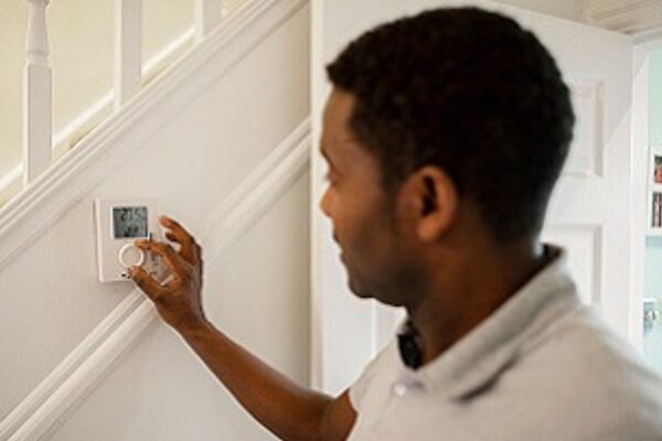 A man adjusting a wall-mounted digital room thermostat on a staircase wall in a home