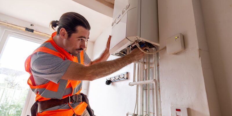 A heating engineer in a high-visibility vest working on a wall-mounted gas boiler in a home