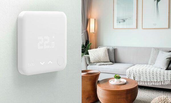 A white tado smart thermostat on a wall showing 22.5 degrees, next to a photo of a grey sofa in a living room