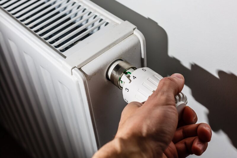 A hand turning the thermostatic radiator valve dial on a white radiator