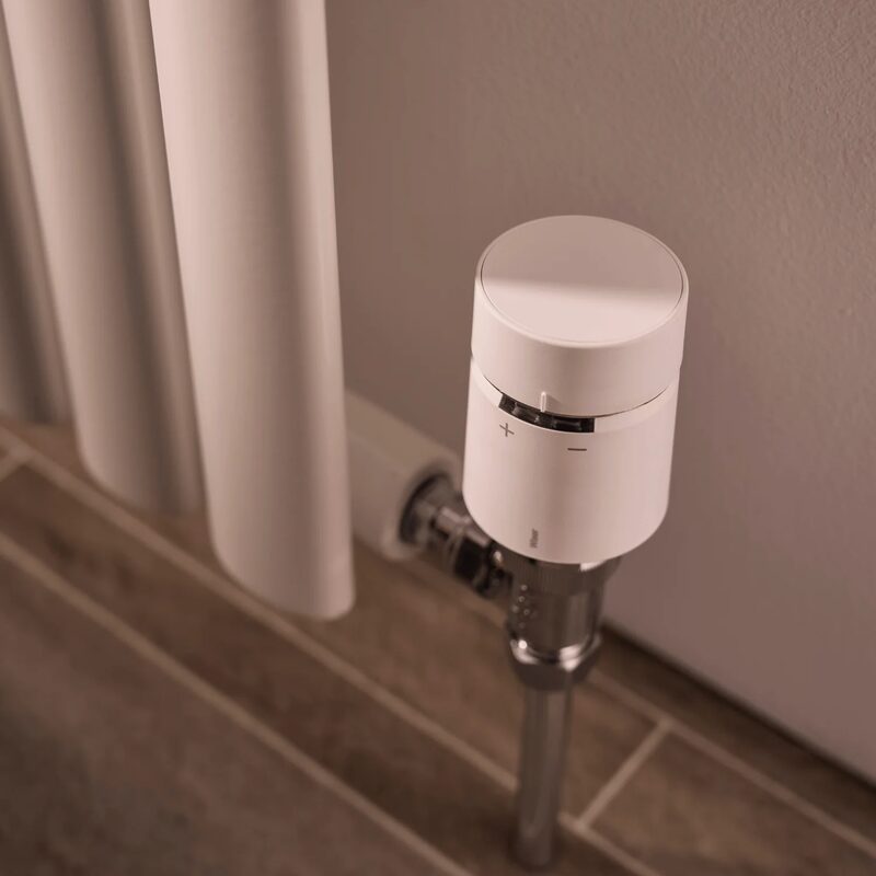 A white Wiser smart radiator thermostat fitted on a radiator valve next to a column radiator