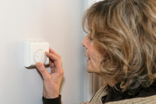 A woman turning the dial on a white wall-mounted room thermostat
