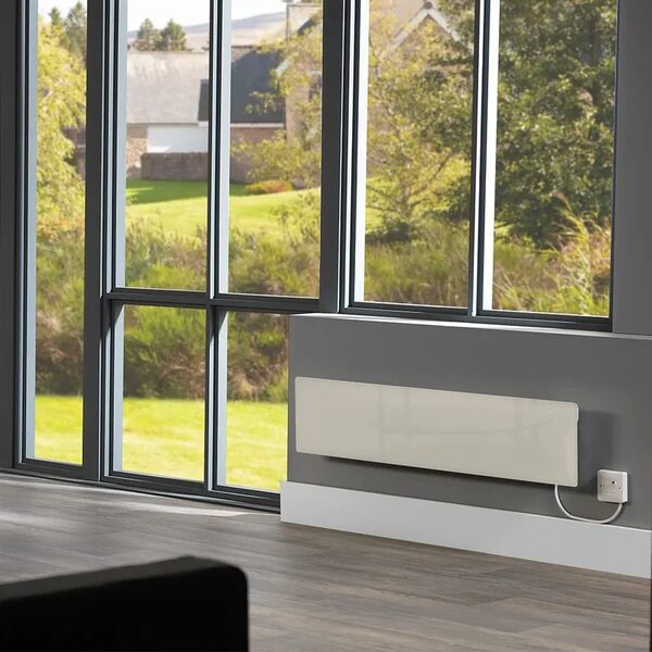 A white glass Dimplex Alta electric panel heater mounted on a grey wall beneath large windows in a modern room