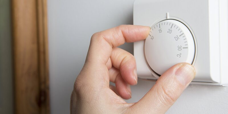 A hand turning the dial of a white wall-mounted room thermostat marked in degrees Celsius