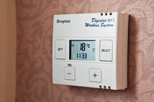 A Drayton Digistat RF3 wireless room thermostat mounted on a patterned wallpapered wall, displaying 18°C