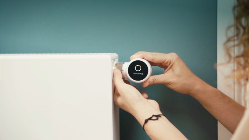 A person screwing a tado° Smart Radiator Thermostat showing 'Mounting' onto a white radiator valve