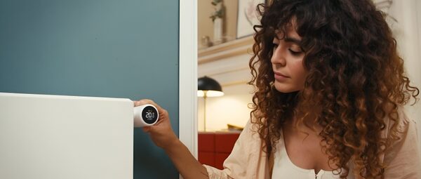 A woman adjusting a tado° smart radiator thermostat on a radiator in a home