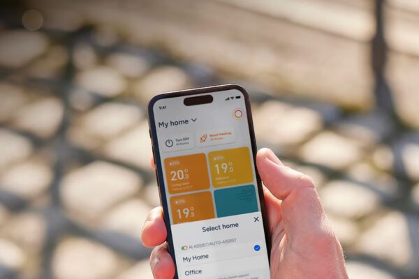 A hand holding a smartphone displaying the tado° smart home control app with room temperatures