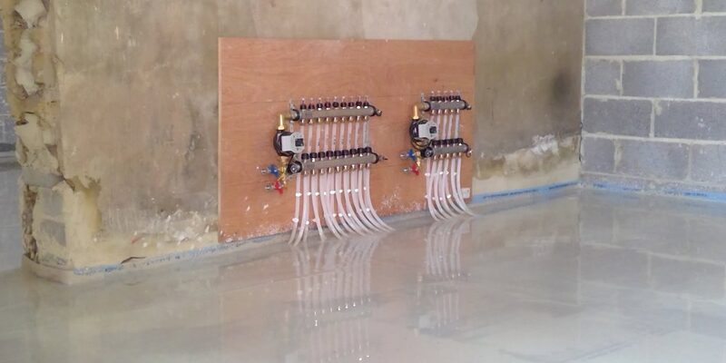 Underfloor heating manifolds with pipe loops mounted on a board in an unfinished room with freshly poured screed floor