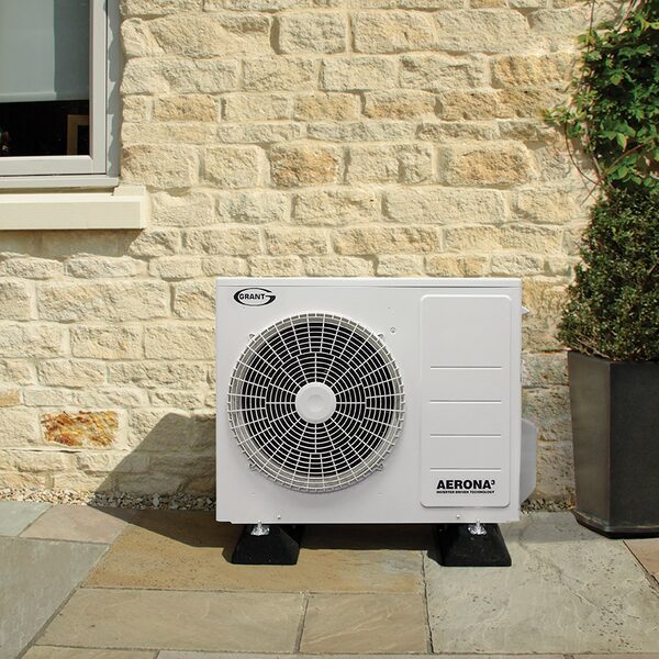 A Grant Aerona³ air source heat pump installed outside a stone house on a paved patio