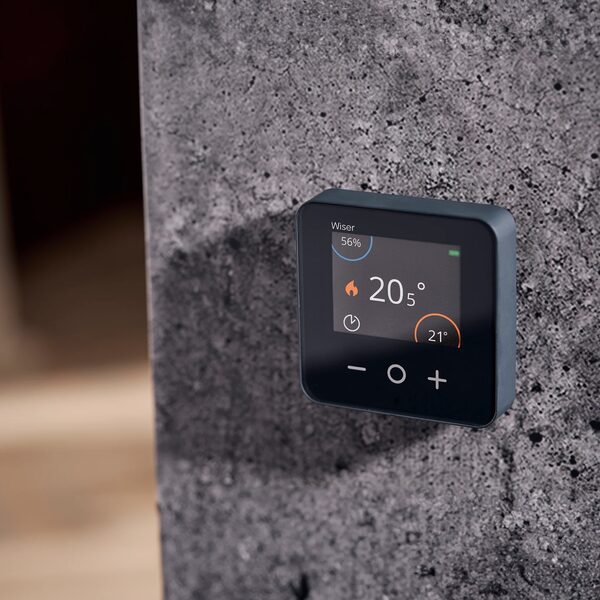 A Wiser smart room thermostat mounted on a concrete wall displaying a set temperature of 20.5°C
