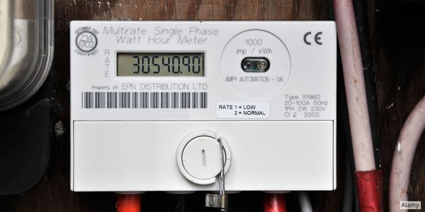 A white multirate single-phase electricity meter with a digital display mounted on a wooden wall with wiring
