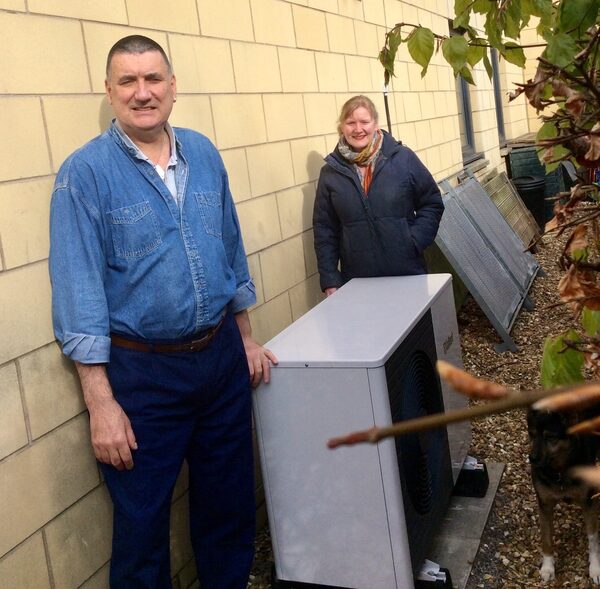 A couple standing beside their air source heat pump unit outside a house wall