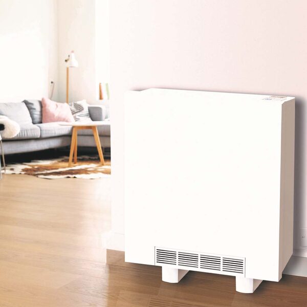 A white Thermastore storage heater installed against a wall in a bright living room with a sofa in the background