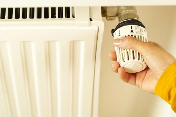 A hand turning the thermostatic radiator valve dial on a white radiator