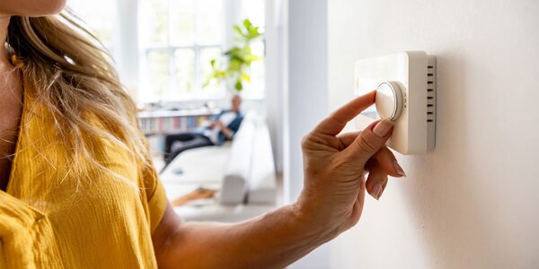 A woman turning the dial on a wall-mounted room thermostat in a bright living room