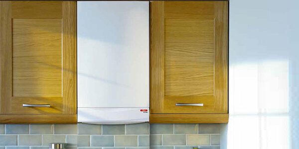 A white wall-mounted combi boiler installed between two oak kitchen cabinet doors above a grey tiled backsplash