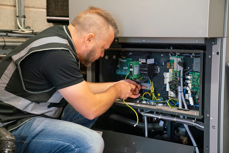 An installer in a hi-vis vest wiring the open control panel of a heat pump unit